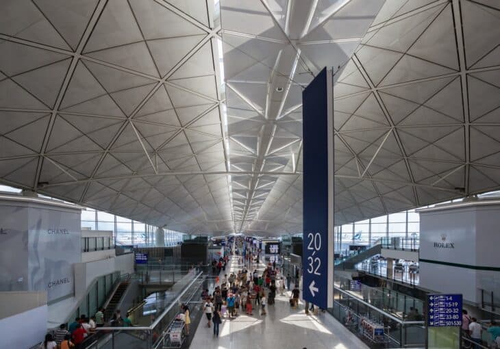 Passengers walking through the vast departures hall at Hong Kong International Airport under a steel roof