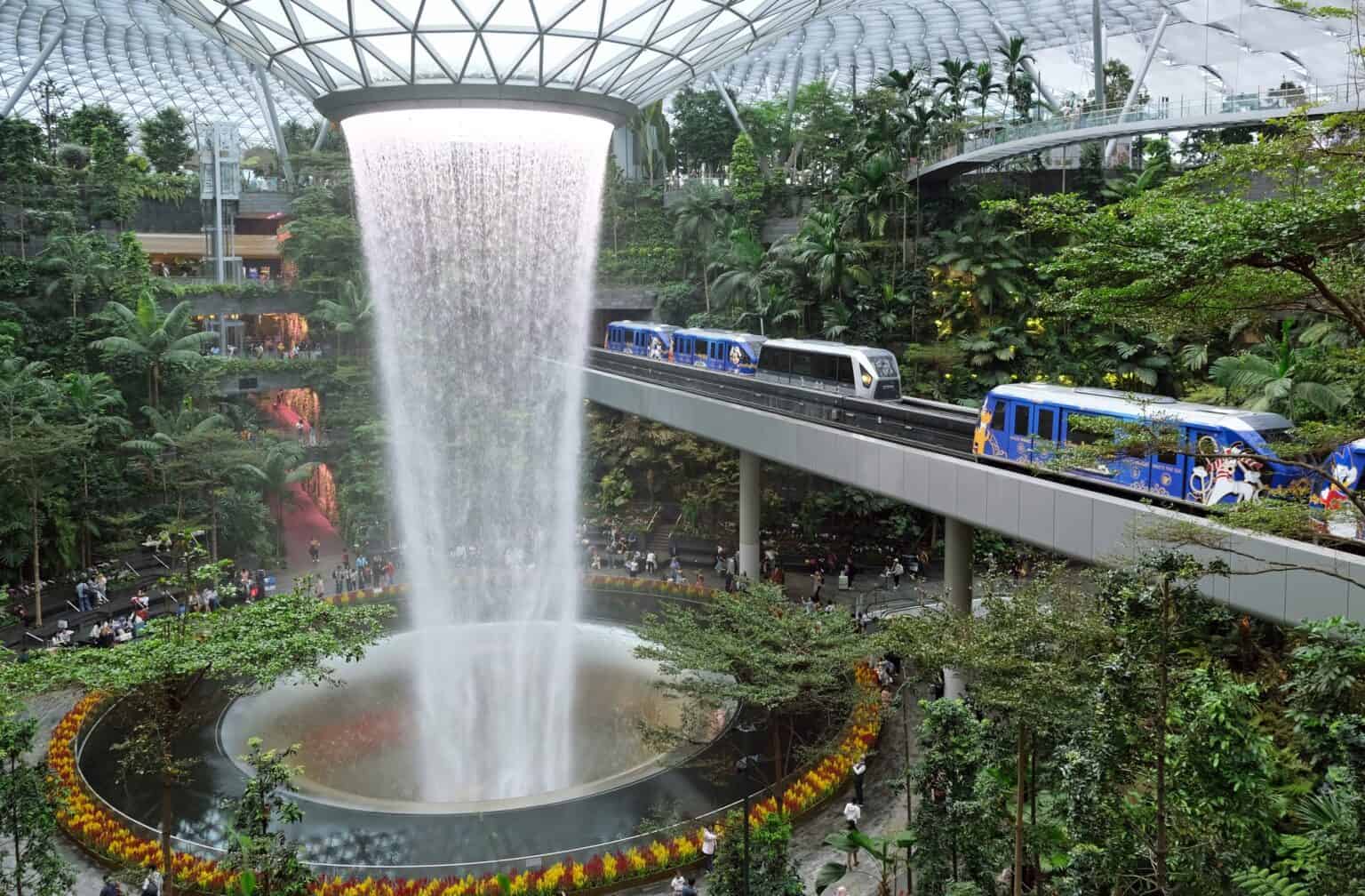 Jewel Changi Rain Vortex waterfall inside Singapore Changi Airport with a Skytrain crossing above the forest