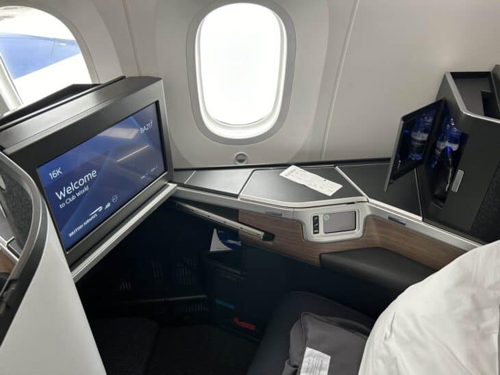 British Airways Club Suite business class seat beside a window, with its entertainment screen and side console, aboard a Boeing 787-10