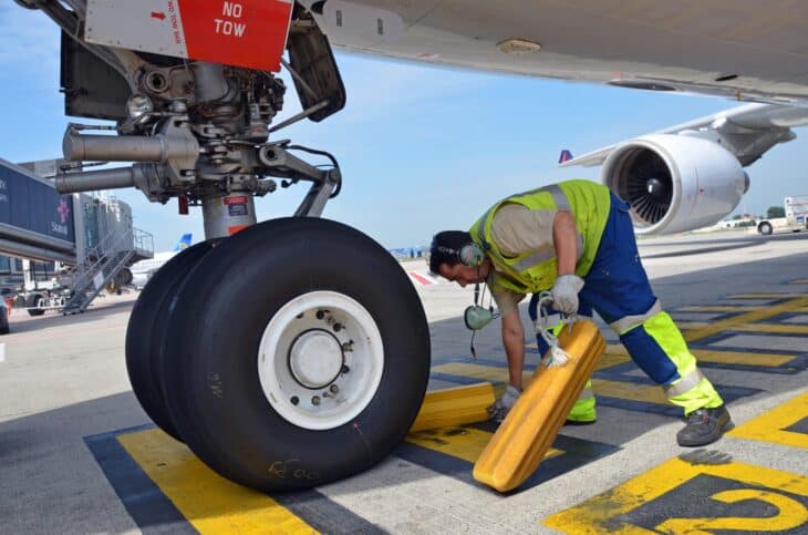Ground worker removing wheel chocks from the nose gear of an Airbus A330 on the ramp at Brussels Airport
