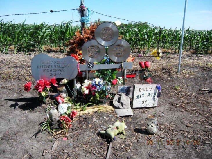 Steel guitar and three metal records memorial surrounded by flowers in a farm field near Clear Lake, Iowa