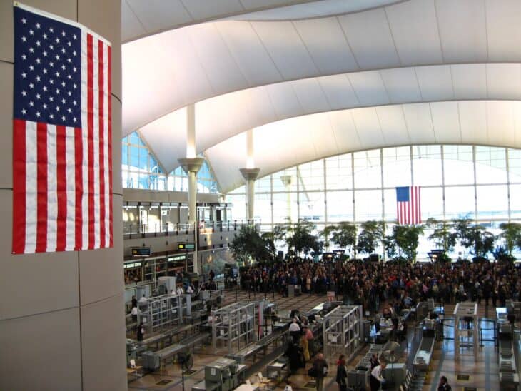 Passengers queuing at the TSA security checkpoint in the Great Hall of Denver International Airport under a hanging American flag