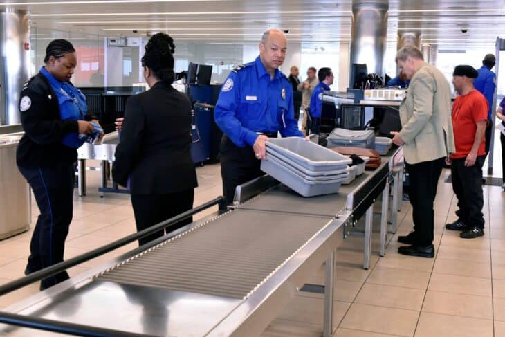 TSA officers stacking bins and screening passengers at an airport security checkpoint