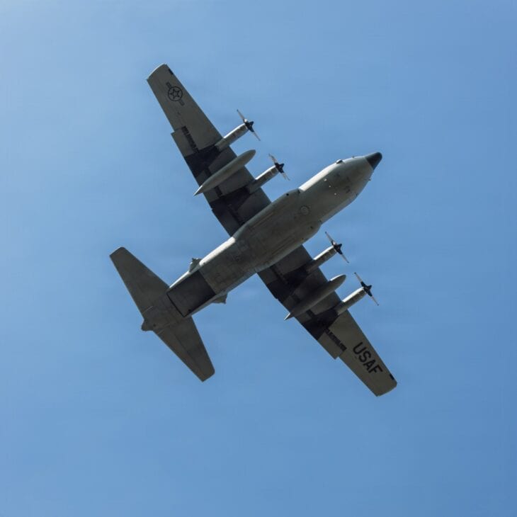 C-130H Hercules seen from below against a blue sky as it flies over a drop zone in Poland