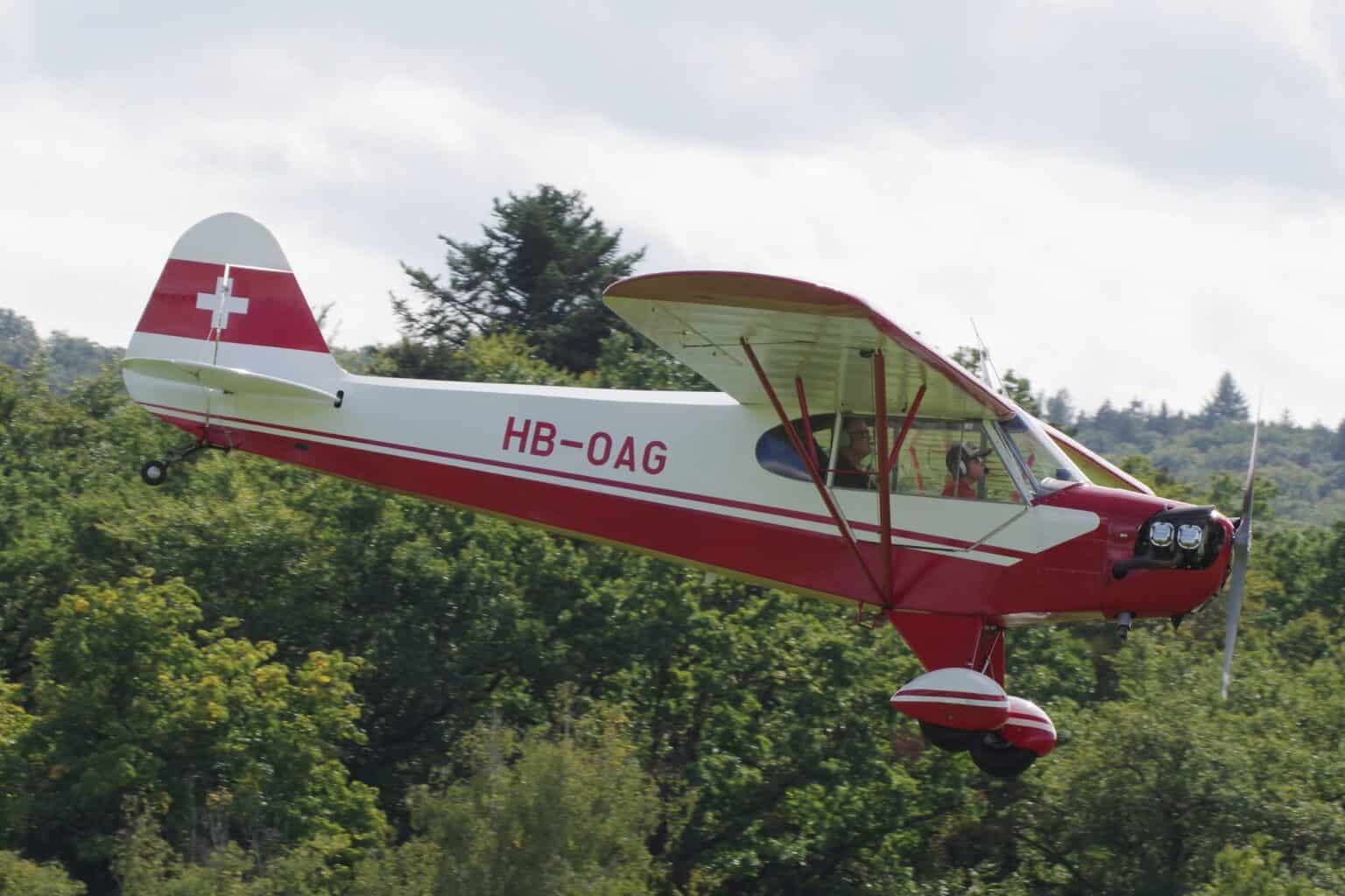 Red and white Piper J-3C-65 Cub HB-OAG flying a low pass over trees