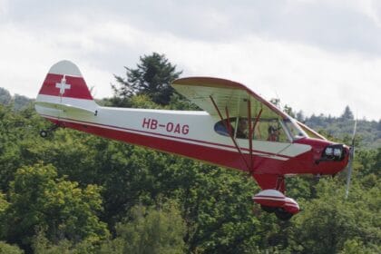 Red and white Piper J-3C-65 Cub HB-OAG flying a low pass over trees