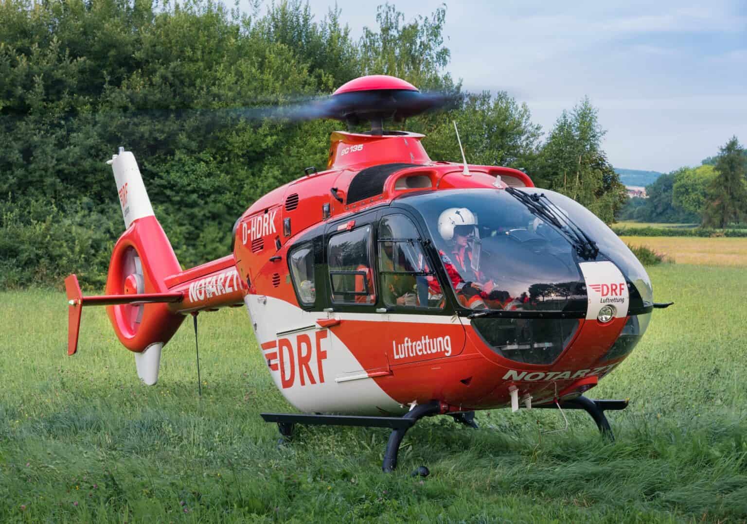 A DRF Luftrettung Eurocopter EC135 air ambulance helicopter in flight over a field, rotor blades blurred