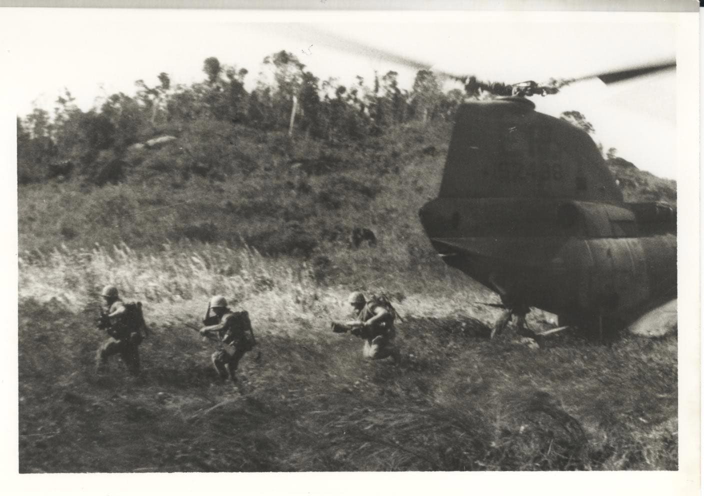 Black and white photo of Marines running through tall grass from a landed CH-46A Sea Knight