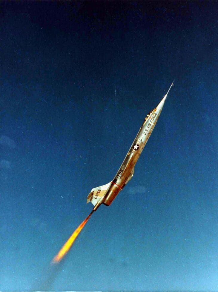 Lockheed NF-104A climbing nose-up with its rocket burning against a deep blue sky