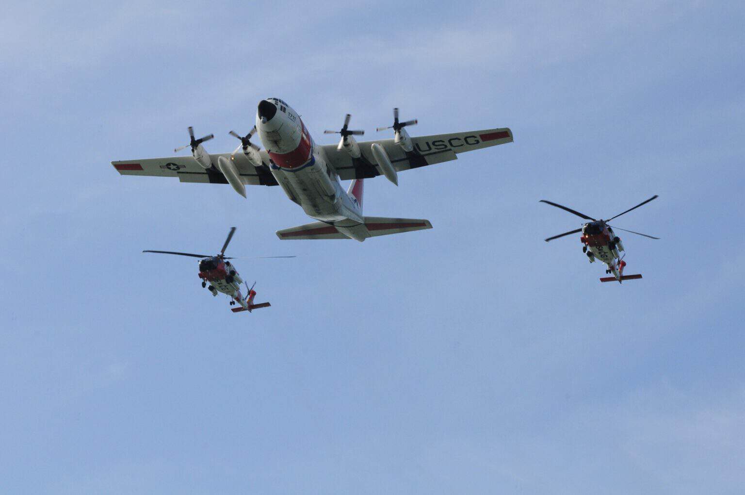 Coast Guard HC-130 Hercules flying in formation with two Coast Guard helicopters over the water