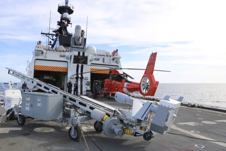 Insitu ScanEagle drone and its launcher on the deck of a Coast Guard cutter beside an MH-65 helicopter