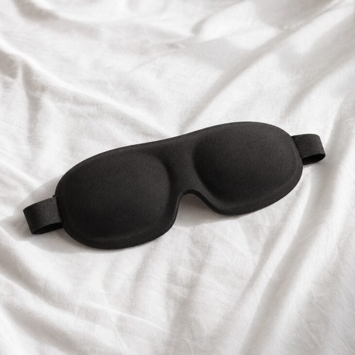 Black contoured sleep mask on white linen