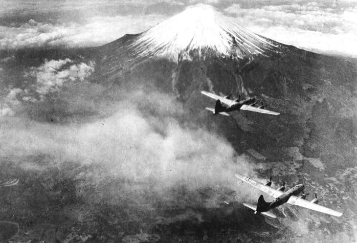 Two B-29 Superfortress bombers flying past Mount Fuji with a smoke plume below