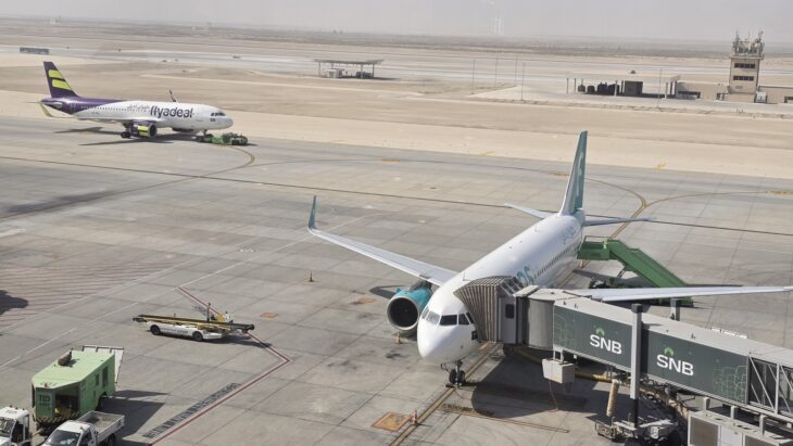 Flynas aircraft at a jet bridge at King Fahd International Airport in Dammam, with a flyadeal aircraft in the background