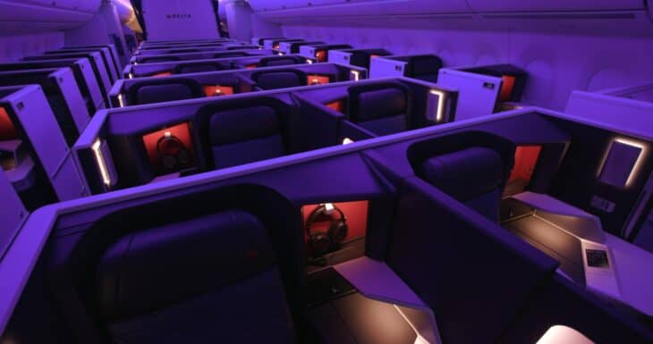 Rows of Delta One Suites with sliding doors on a Delta Airbus A350, lit in purple cabin lighting
