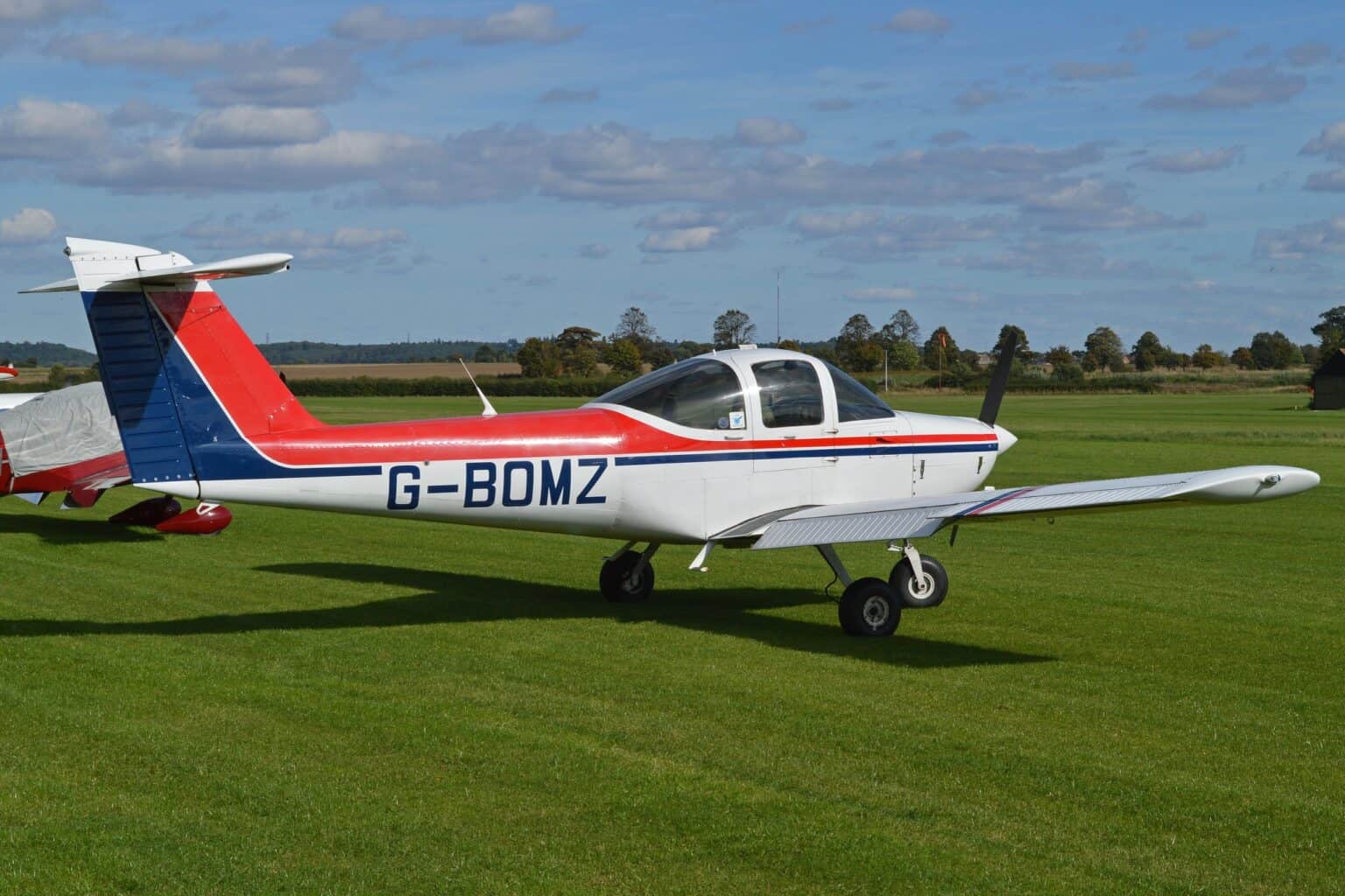Piper PA-38 Tomahawk G-BOMZ taxiing on a grass airfield in red, white and blue livery