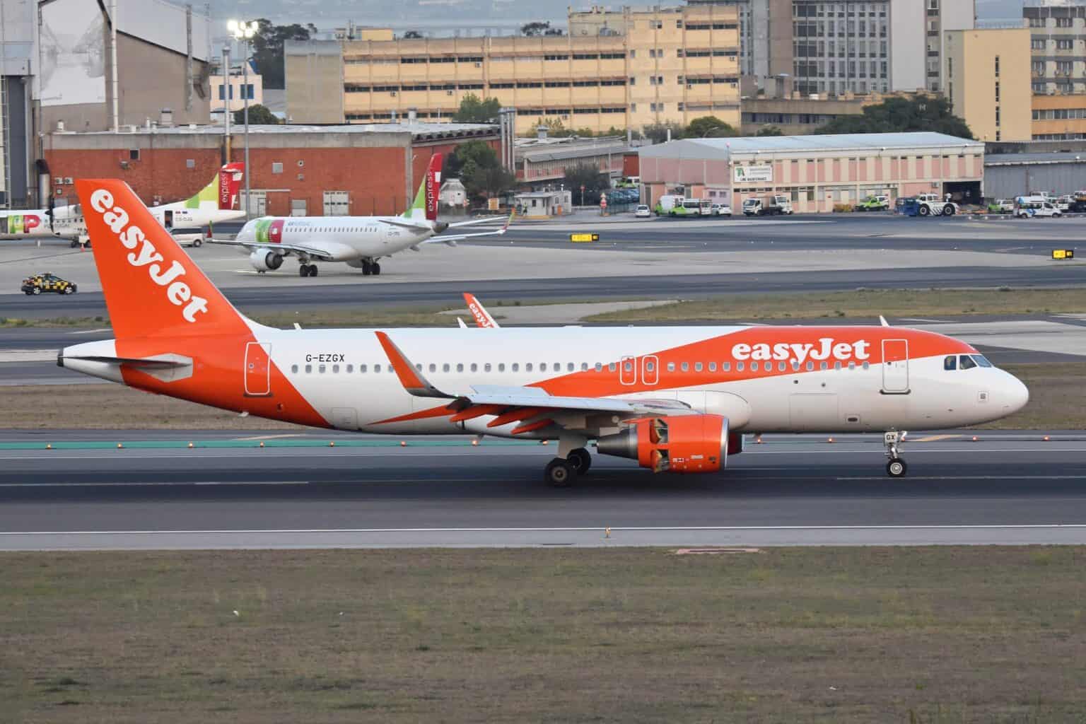 easyJet Airbus A320 G-EZGX on the runway at Lisbon Humberto Delgado Airport, with TAP Air Portugal jets parked behind