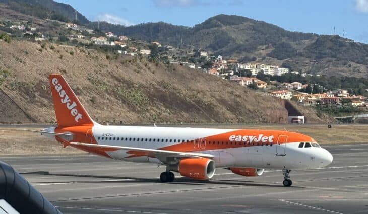 easyJet Airbus A320 taxiing at Madeira Airport in Funchal, with steep green hillsides and houses behind the runway
