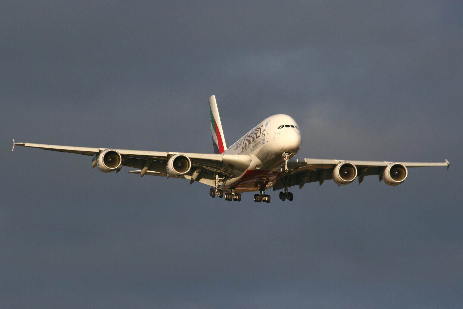 Emirates Airbus A380 A6-EDX on final approach with its landing gear down, lit by low sun against a dark sky