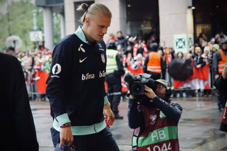 Erling Haaland in a Norway team jacket with his hair tied back, walking through a crowd in Oslo