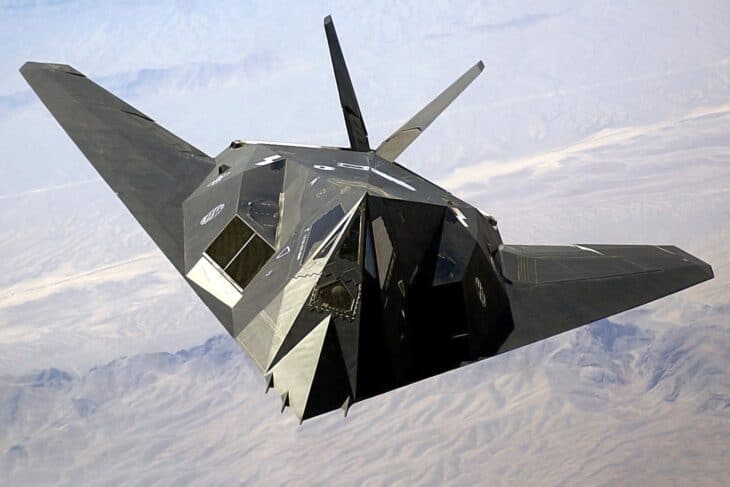 F-117A Nighthawk banking over desert terrain, seen from above and ahead