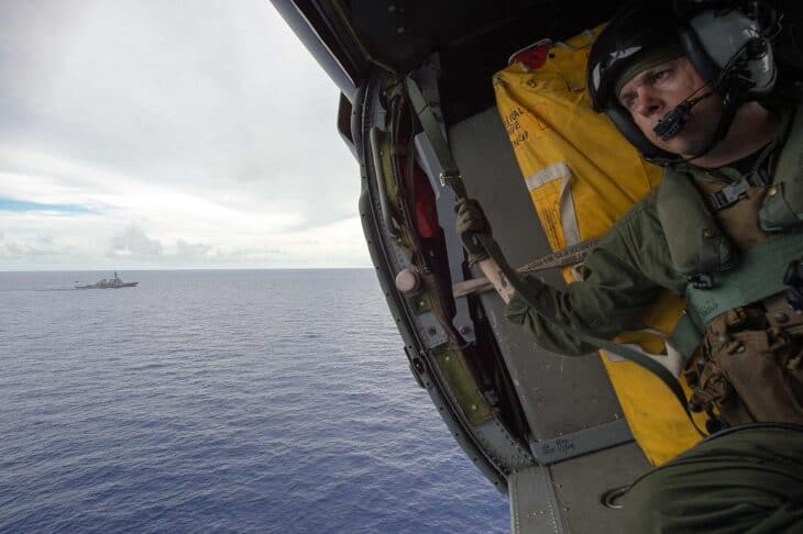 Crew member operating a rescue hoist at the open door of a US Navy helicopter over the sea