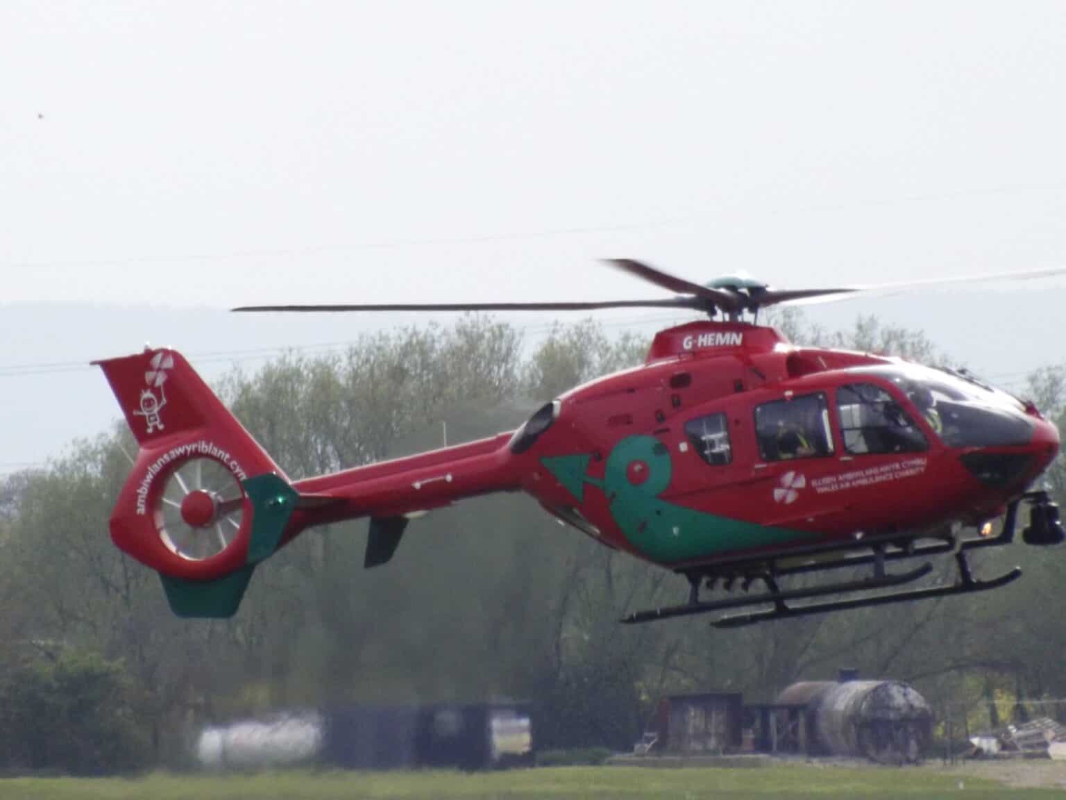 Red Eurocopter EC135 air ambulance helicopter G-HEMN hovering low over a grass field