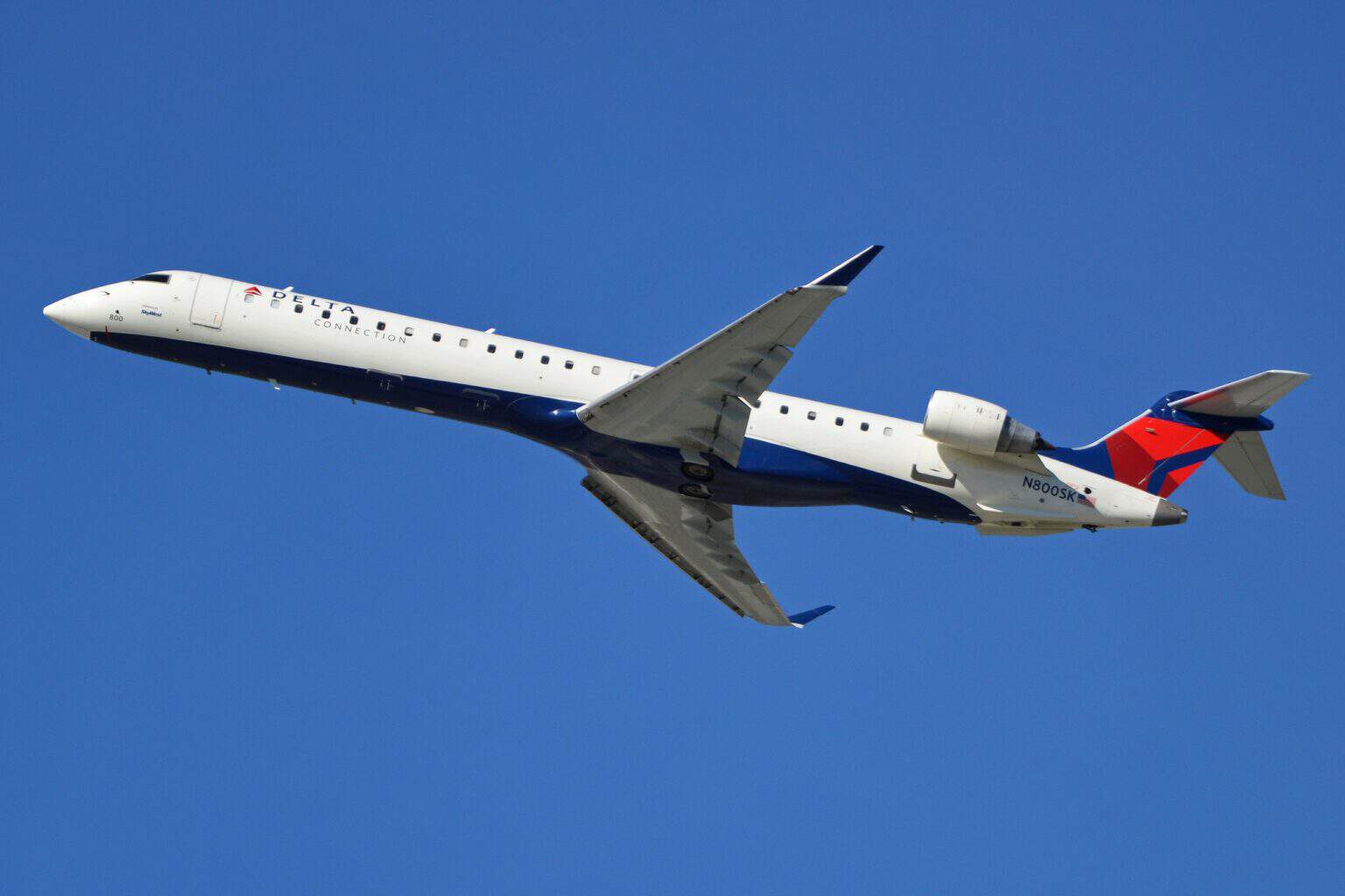 Delta Connection Bombardier CRJ900 climbing out against a blue sky, its two rear-mounted engines visible