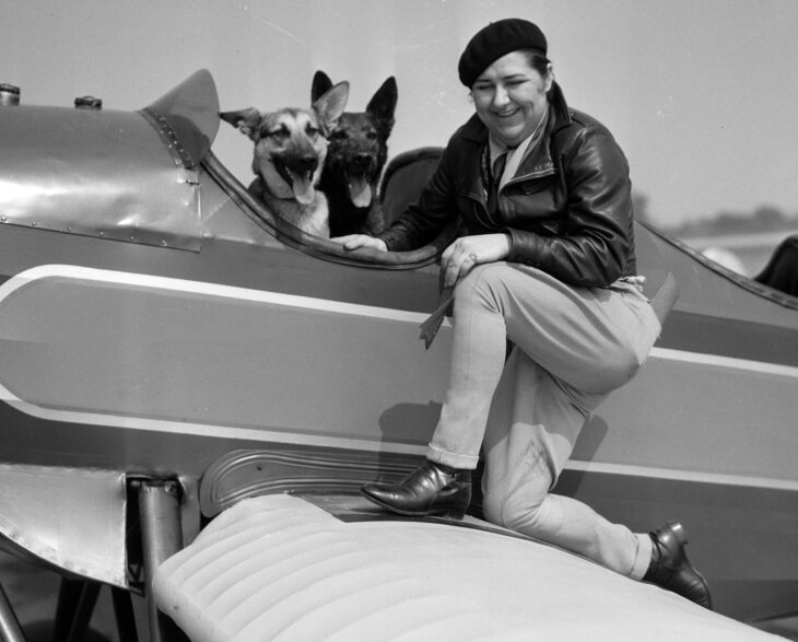 Pancho Barnes sitting on the wing of a biplane with her dogs in 1931