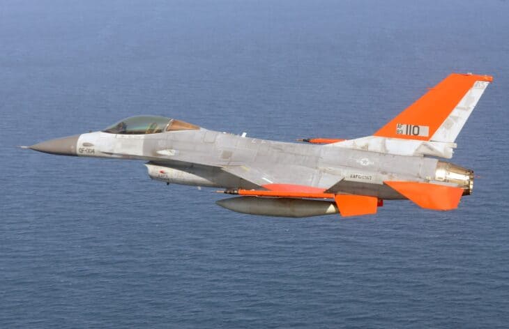 Boeing QF-16 target drone with an orange tail flying low over the sea