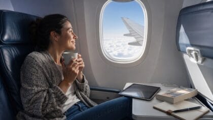 Adult traveler's tablet, paperback and notebook on an airplane tray table