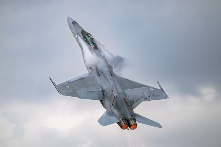 Finnish Air Force F/A-18C Hornet pulling up in a steep climb with vapour streaming off the wings and afterburners lit