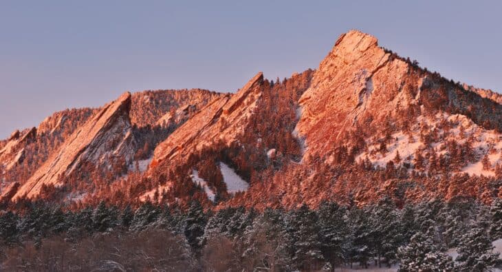 The Flatirons rock slabs above Boulder, Colorado, lit orange at sunrise, seen from Chautauqua