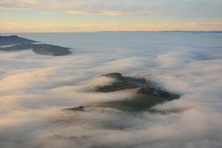 A thick white layer of fog filling a valley below a hilltop at sunrise