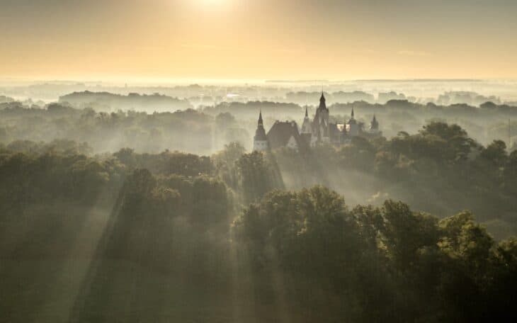 Morning mist among the forests around Moszna Castle in Poland, with the castle and distant treetops still visible