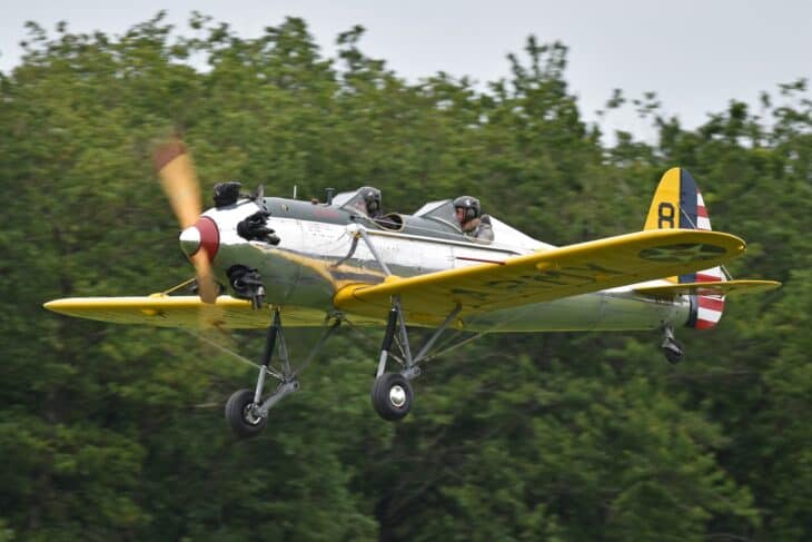 Ryan PT-22 Recruit N53018 with yellow wings and a tail marked 8 climbing out just above the treeline