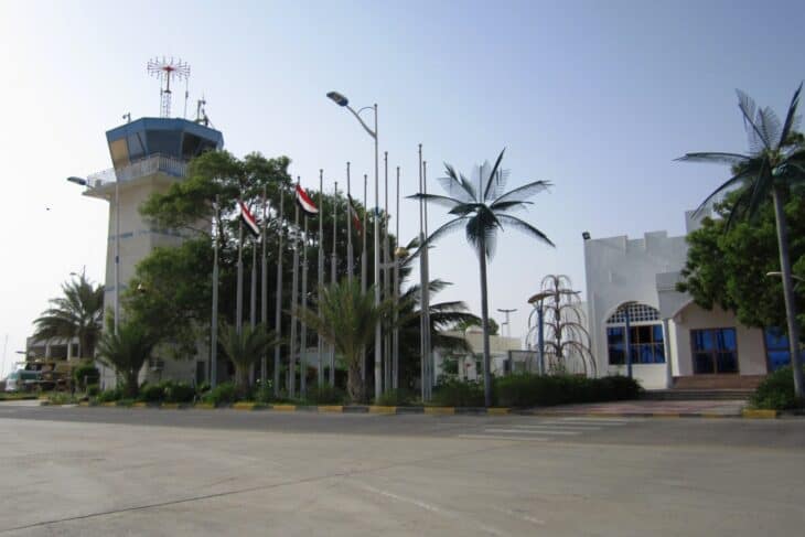 Control tower and terminal building at Riyan airport near Mukalla, Yemen, with palm trees and a row of flagpoles