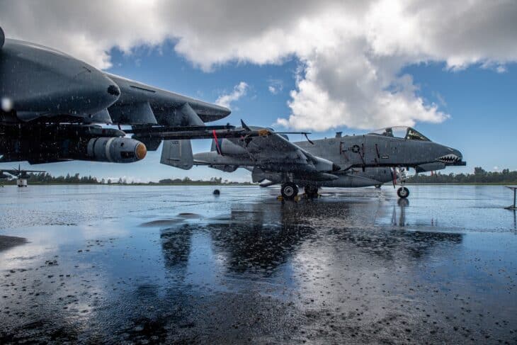 Two A-10C Thunderbolt II jets parked on a rain-soaked ramp under broken cloud in Palau