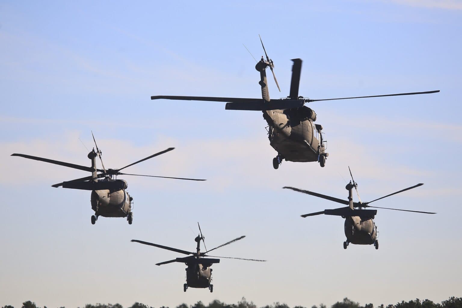 Four US Army UH-60 Black Hawk helicopters flying in formation against a pale sky