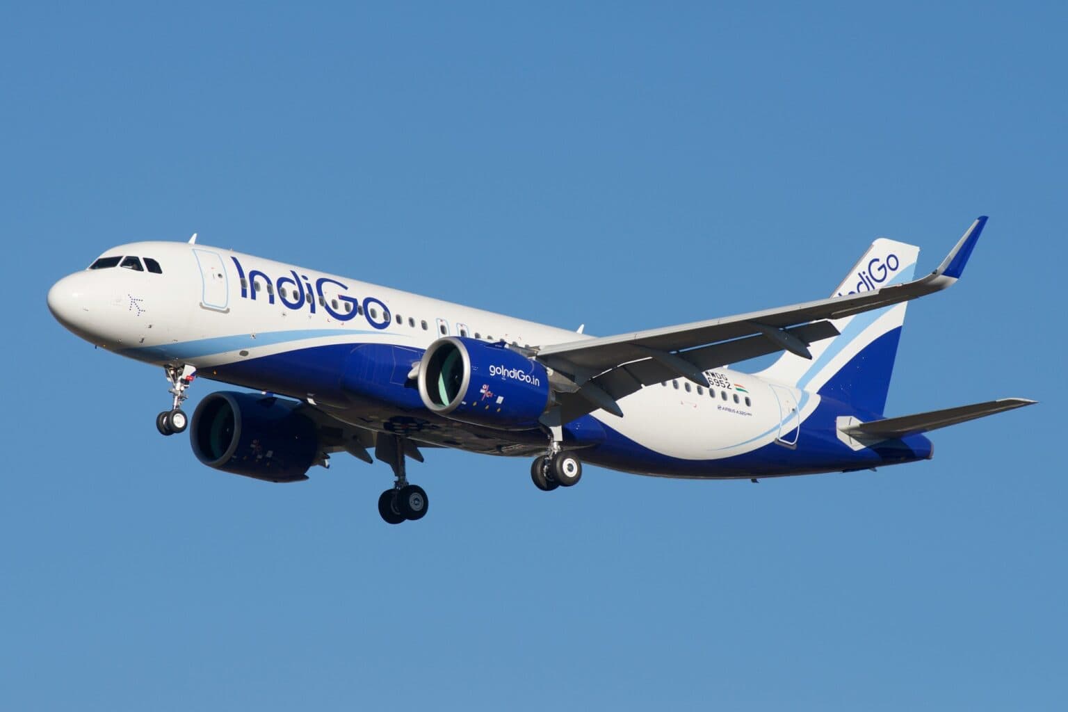 IndiGo Airbus A320neo on final approach with landing gear down against a clear blue sky