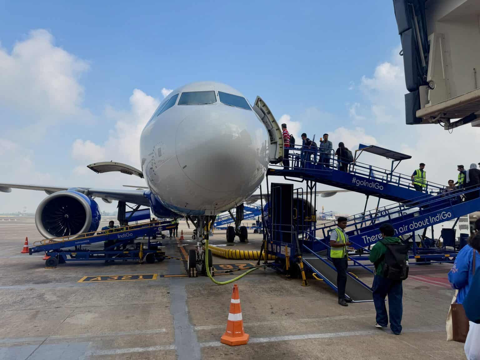 IndiGo Airbus A321neo parked on a stand with passengers carrying bags up two mobile airstairs
