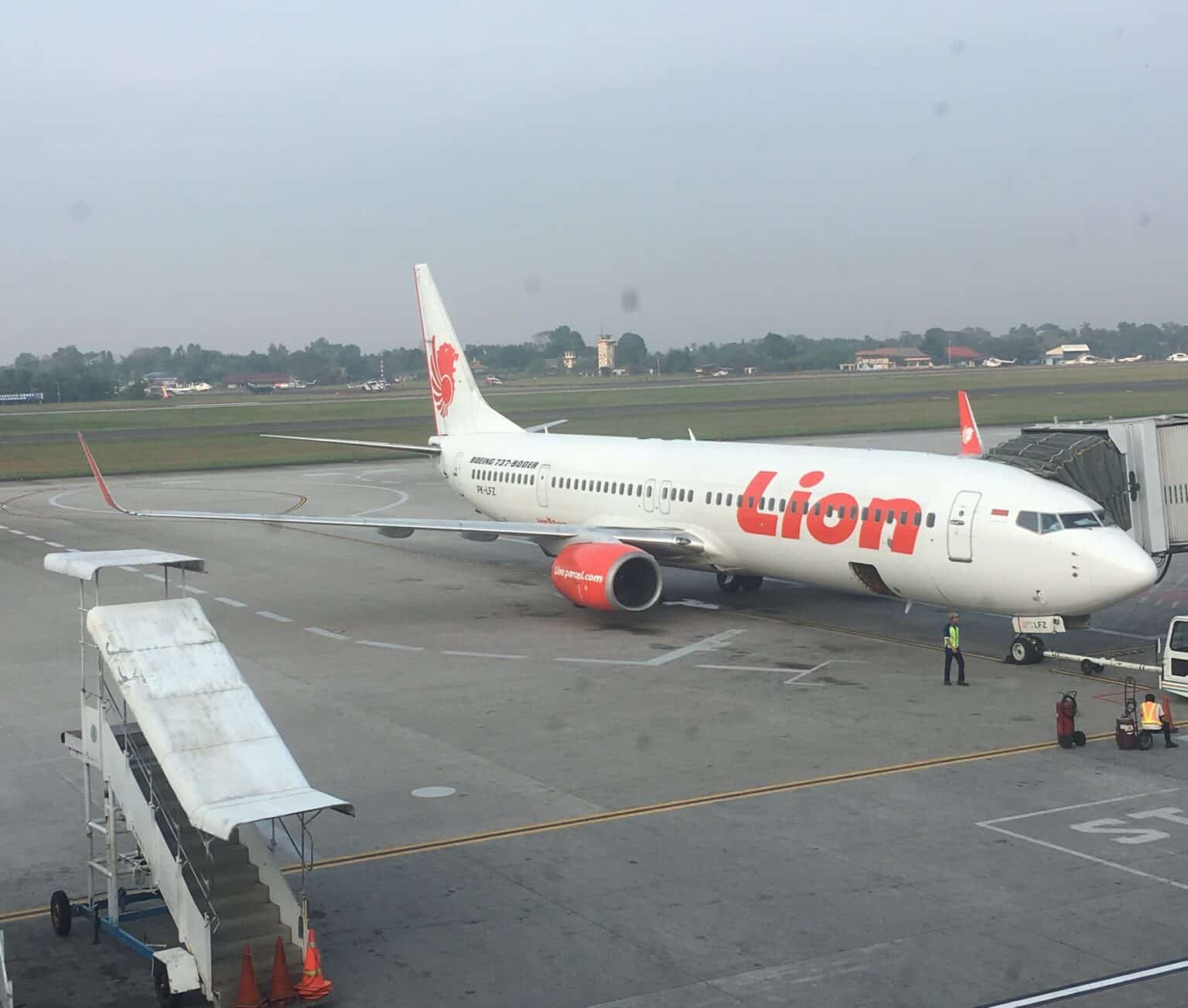 Lion Air Boeing 737-900ER parked at a gate at Palembang's Sultan Mahmud Badaruddin II Airport under a hazy grey sky
