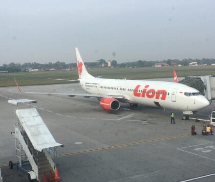 Lion Air Boeing 737-900ER parked at a gate at Palembang's Sultan Mahmud Badaruddin II Airport under a hazy grey sky
