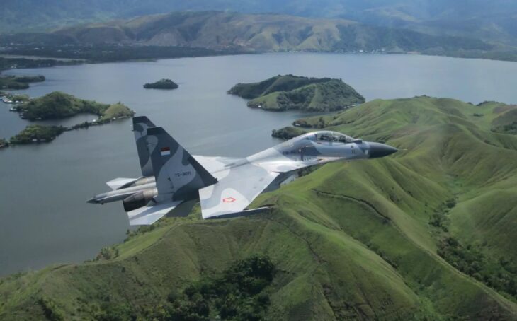 Indonesian Air Force Su-30 flying over green hills and an island bay
