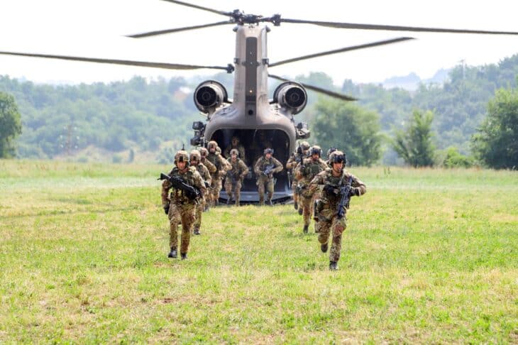 Italian Army soldiers running out of the rear ramp of a Chinook helicopter onto a grass field