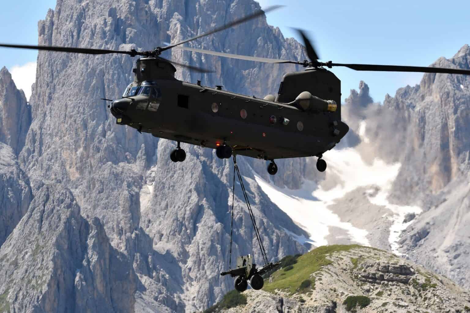 Italian Army CH-47F Chinook carrying a slung load past a rocky mountain face during an exercise