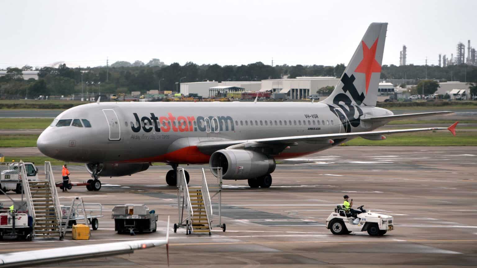 Jetstar Airbus A320 VH-VGR taxiing at Brisbane Airport as ground crew work nearby with stairs and equipment