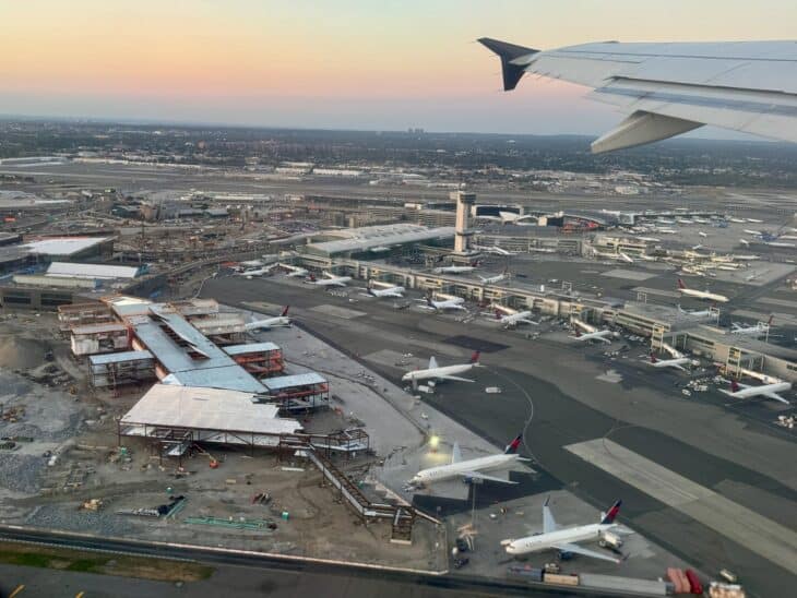 Aerial view of JFK Airport terminals and aircraft at sunset, seen from an airliner wing