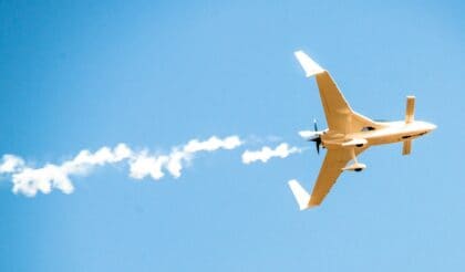 Rutan Long-EZ banking overhead against a clear blue sky, trailing a white smoke-system plume