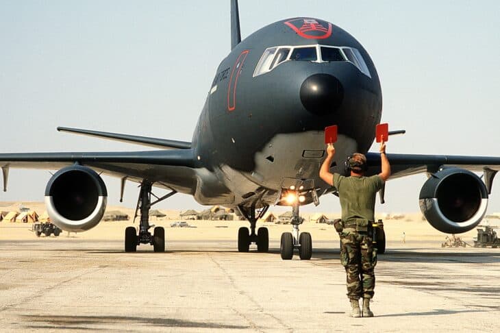 Ground crew member guiding a KC-10A Extender into a parking spot, nose-on view